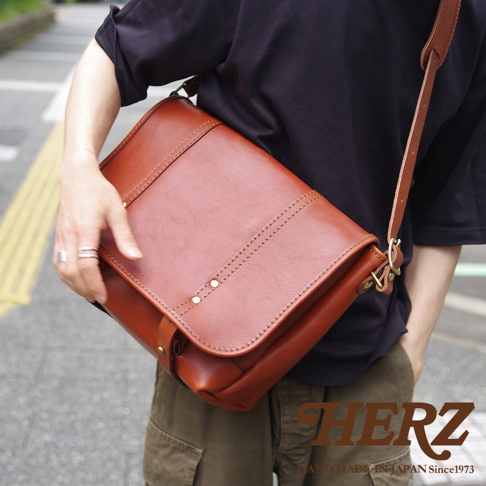 職人手作皮革復古郵差包，經典棕色，採用厚實真皮材質，帶有精緻的縫線及鉚釘裝飾，款式簡約實用，適合日常搭配。