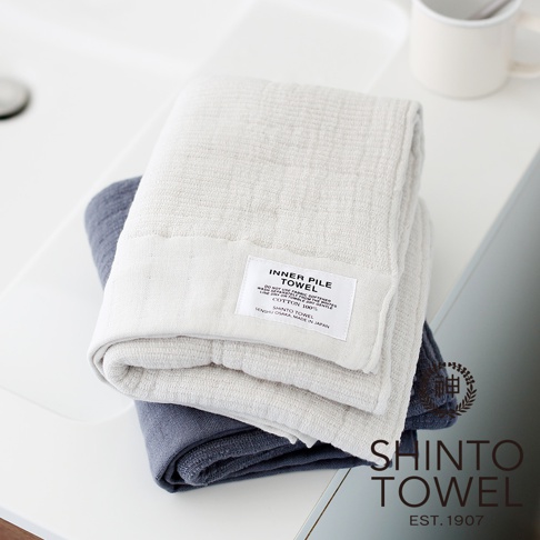 疊放的雙面紗布輕質浴巾，上方為淺米色，下方為藍灰色。兩條浴巾均為純棉材質，質地輕柔，呈現出細緻的紋理。