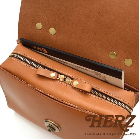 HERZ 職人手作皮革多功能收納單肩包，棕色皮革，特寫內部收納空間與拉鍊細節，底部有 HERZ 品牌標誌及「HAND MADE IN JAPAN since1973」文字。