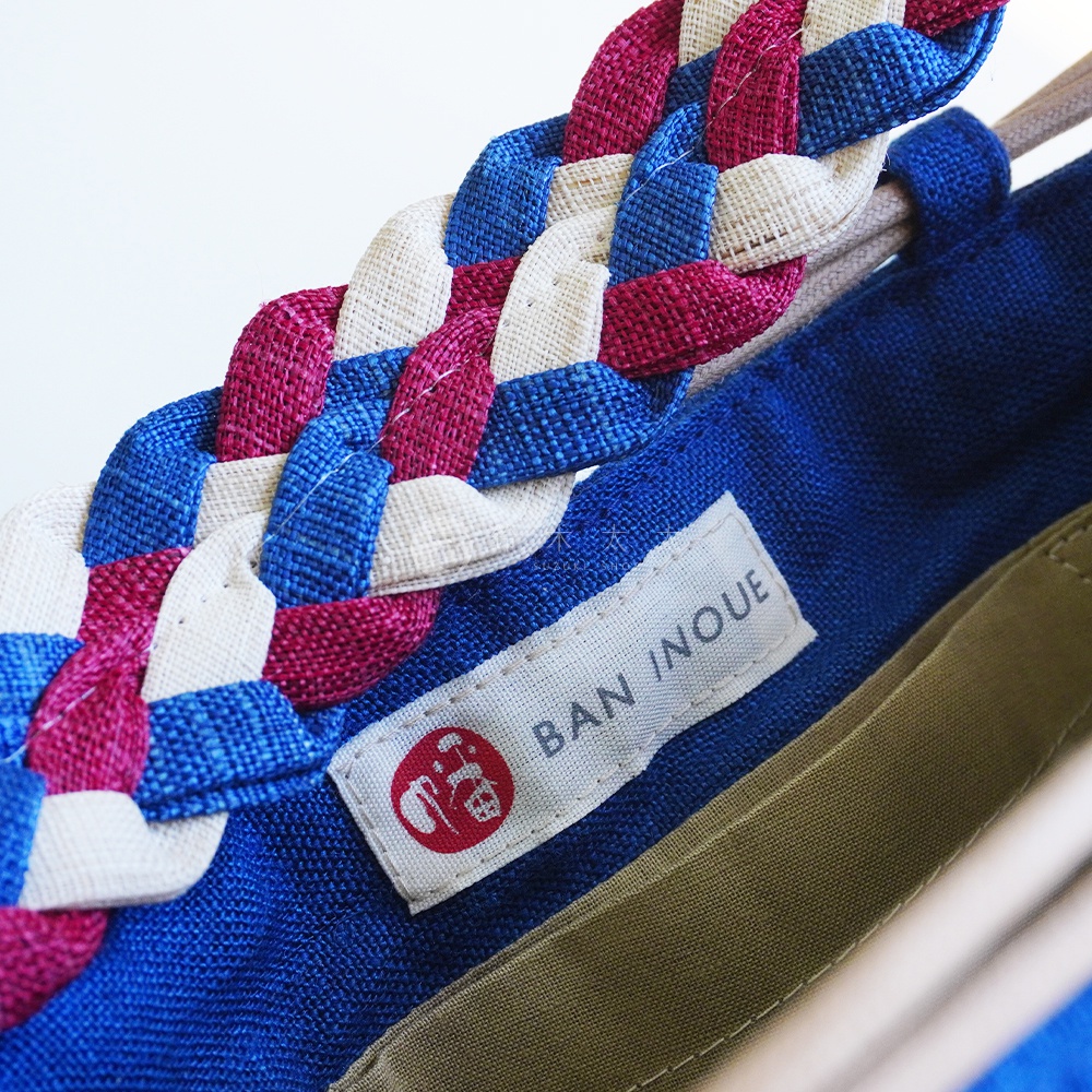 BAN INOUE 手提包的編織提把，由粉紅色、藍色和米白色織帶交織而成。