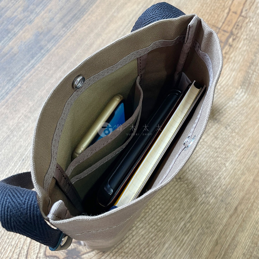 包包內部有手機、筆記本和文件夾，帆布材質，米色內襯，黑色揹帶。