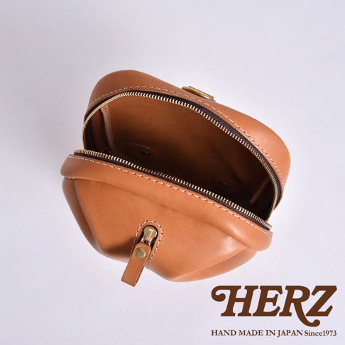 HERZ 標誌旁的手工皮革立體運動斜背包，露出內部，拉鍊細節清晰可見