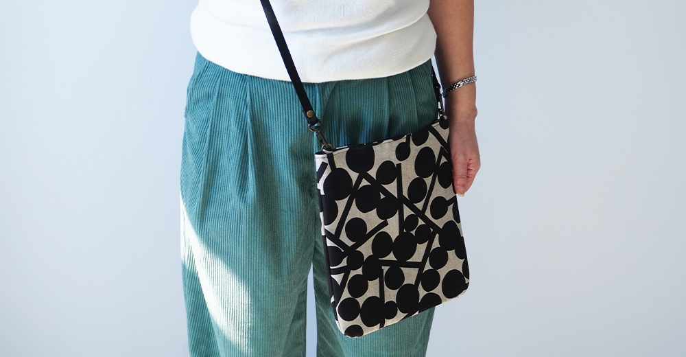 BAN INOUE 自然織紋麻布斜背包 (果實花紋)，黑色與米色幾何圖案，搭配淺綠色燈芯絨長褲