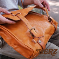 職人手作皮革水洗加工復古郵差包，呈現天然焦糖色澤，質感柔軟，配有可調節的皮革背帶及金屬扣環，風格簡約。