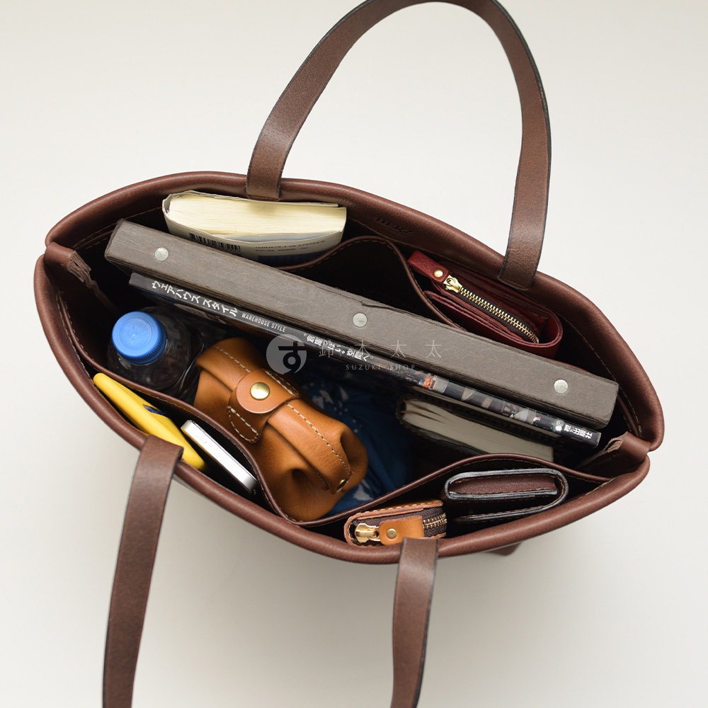 深棕色職人手作皮革托特包，內部可見多個隔層，裝有書籍、水瓶、手機、皮夾及其他小物。