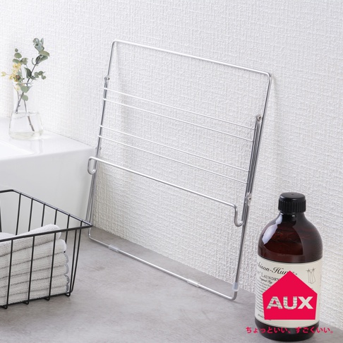 金屬網格折疊式晾曬架，帶有多層晾衣桿，可懸掛衣物。旁邊有一個黑色網籃，裡面裝有疊好的白色毛巾，以及一瓶深棕色液體的瓶子。