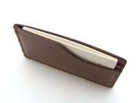 深棕色皮革製成的手工卡片夾，夾有白色卡片，邊緣縫線明顯。