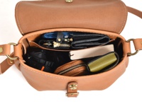 棕色皮革馬鞍包，內部裝有藍色錢包、鑰匙包、黑色相機、書本和綠色小皮夾。包款配有黃銅色金屬扣環和可調節肩帶。