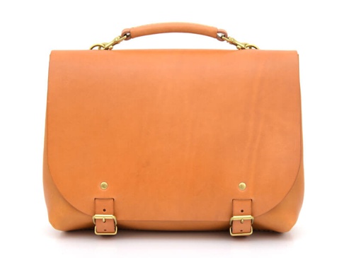 棕褐色皮革雙扣兩用側背包，設有頂部提把，以黃銅色金屬扣環和铆釘固定，風格簡潔。