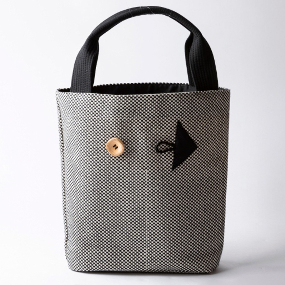 三河木綿刺子織製成的直式收納托特包，以黑白格紋布料製作，頂部有黑色提把，包身正面有一個木質鈕扣和一個黑色的箭頭造型裝飾。