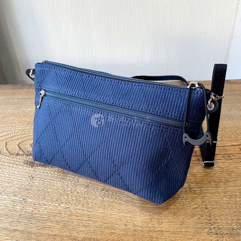 深藍色刺子織紋隨身斜背包，側面有拉鍊口袋，附有可拆卸的黑色背帶和一個黑色小裝飾。