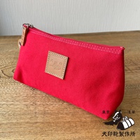 紅色石洗帆布小物收納包，採用拉鍊開合，正面有一個方形皮革標籤，上面壓印有圖案和文字。