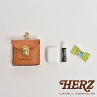 職人手作皮革耳機收納包 KF-4，淺棕色皮革，附黃銅鎖扣及掛鉤，旁為白色無線耳機、藥用護唇膏及綠色糖果。