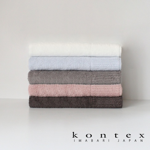 堆疊著五條不同顏色的浴巾，從上至下分別為白色、淺藍色、灰色、粉紅色和深棕色。浴巾質地蓬鬆柔軟。