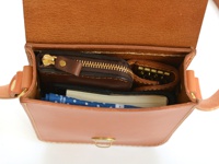 職人手作皮革經典皮扣單肩包 (CP-97)，打開的淺棕色皮革包內，可見一個深棕色拉鍊零錢包、一個金色鑰匙圈，以及一本筆記本和藍色印花布。