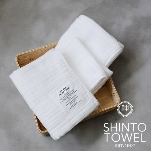 籃子裡疊放著三條純白色2.5層紗浴巾，材質柔軟，表面有細緻的織紋。