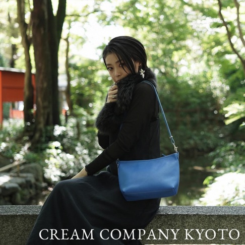 藍色皮革手提側背包，簡約方形設計，配有細長可調式肩帶，適合日常攜帶。