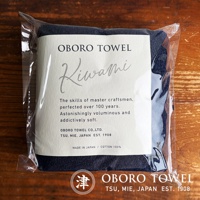 深藍色細纖浴巾，以透明包裝袋展示，標籤上有「OBORO TOWEL KIWAMI」字樣，並說明「MADE IN JAPAN / COTTON 100%」。