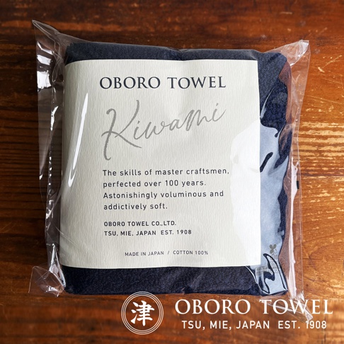 深藍色細纖浴巾，以透明包裝袋展示，標籤上有「OBORO TOWEL KIWAMI」字樣，並說明「MADE IN JAPAN / COTTON 100%」。
