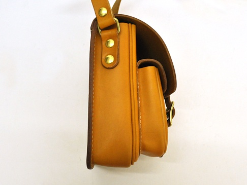 側視圖，職人手作的黃褐色皮革直式單肩包，附有金屬釦和皮革翻蓋。