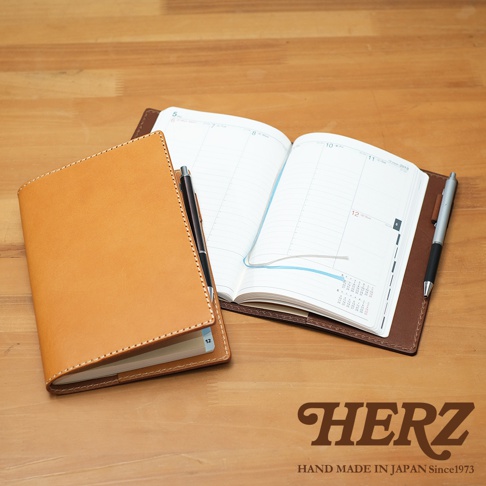 職人手作皮革B6記事本書套，淺棕色皮革封套，內含一本展開的日誌，筆記本旁有黑色與銀色鋼筆。