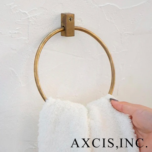 輕奢黃銅圓形毛巾環，固定在白色紋理牆面上，環體呈現金屬光澤，下方掛著一條蓬鬆的白色毛巾，一隻手正將毛巾掛上。