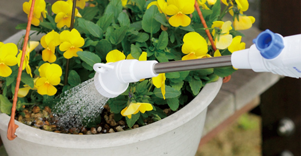 短灑水噴嘴 QG138FJ，白色塑膠噴頭搭配金屬管，藍色旋鈕，正在為盆栽中的黃色三色堇澆水。