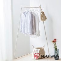 角落造型吊掛衣桿，白色金屬支架，懸掛多件條紋及素色襯衫，右側吊掛一個米色帆布袋，下方放置編織籃及鮮花。