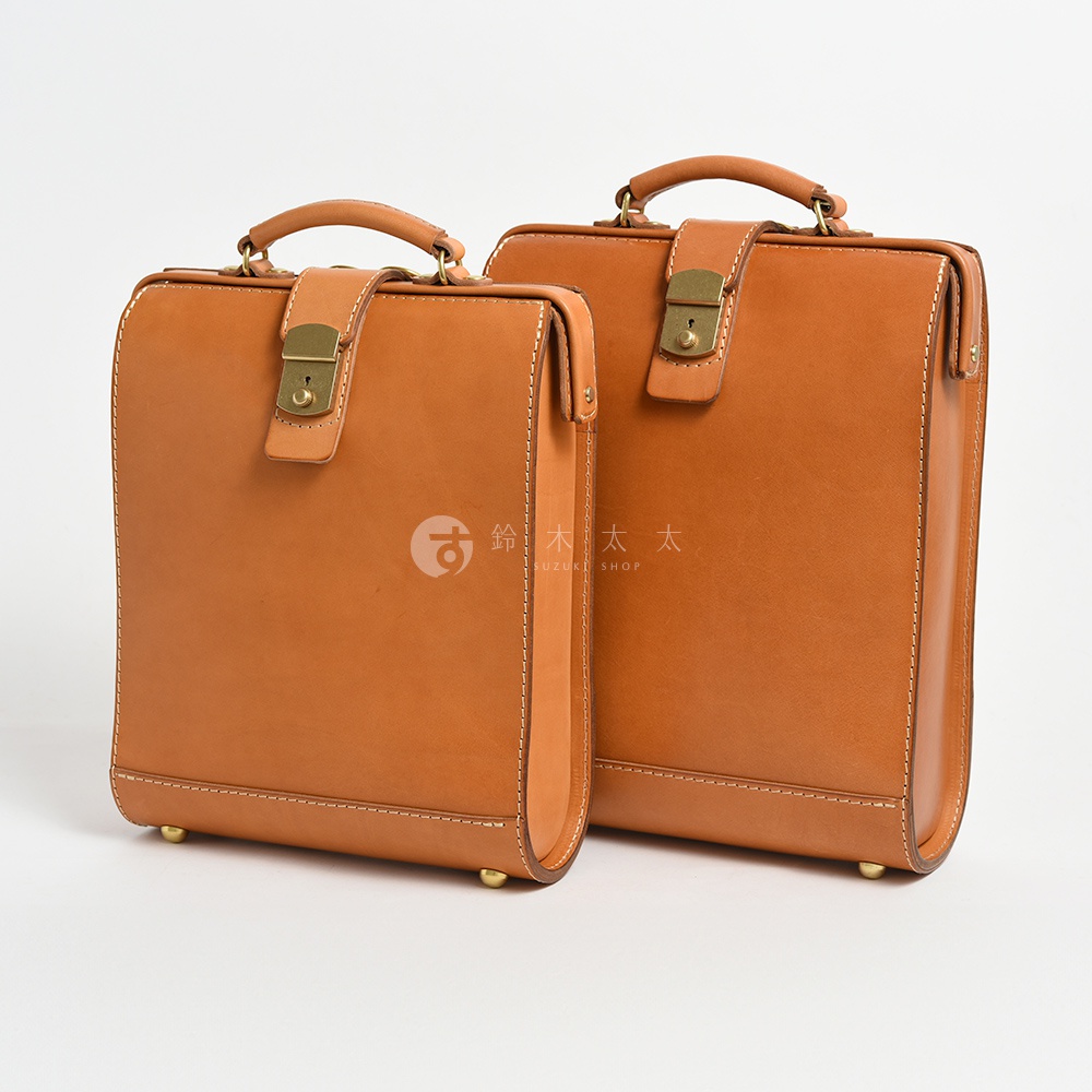 兩款棕色皮革製的商務後背包，皆有頂部提把、鎖扣和金屬腳釘，其中一款較小。