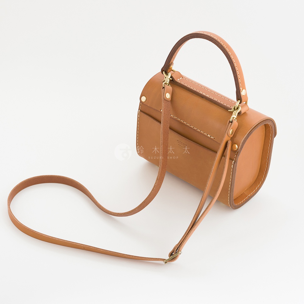 職人手作皮革復古杜勒斯手提包，採用天然皮革製成，呈現溫潤的焦糖棕色。包身為圓筒狀，配有可拆卸的短提把及長肩帶，側面設有兩個插袋，整體設計簡約而經典。