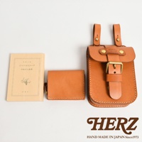 棕色皮革腰袋，帶有黃銅扣環和皮帶。旁邊有一個小巧的棕色皮革錢包和一本淺黃色封面書籍，書名為「ジャイロスコープ」。