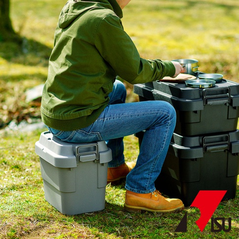 灰色的 TRUNK CARGO 可堆疊收納箱，配有黑色扣環，置於戶外草地上。箱子由耐用的塑膠製成，表面光滑，頂部可作為簡易座椅。