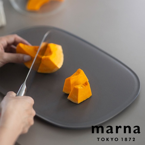 marna TOKYO 1872 品牌標誌旁，一隻手正在用刀將南瓜切塊，旁邊還有兩塊切好的南瓜，放置在灰色的砧板上