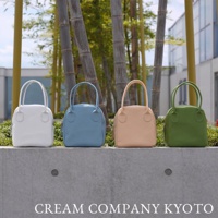 四款皮革手提包，分別為白色、淺藍色、米色和綠色，皆為貝殼造型，配有兩條短提把，置於戶外水泥平台上。