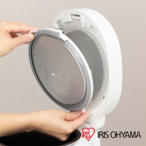 一張白色電鍋打開蓋子的特寫，一隻手正將內蓋取下，內蓋是銀色的，上面有許多圓點和一些標示。