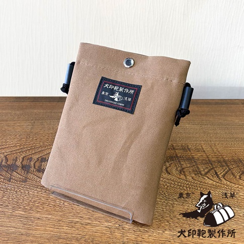 犬印鞄製作所米色帆布手機包，上面有一個黑色標籤，印有「犬印鞄製作所」、「東京」、「淺草」字樣。