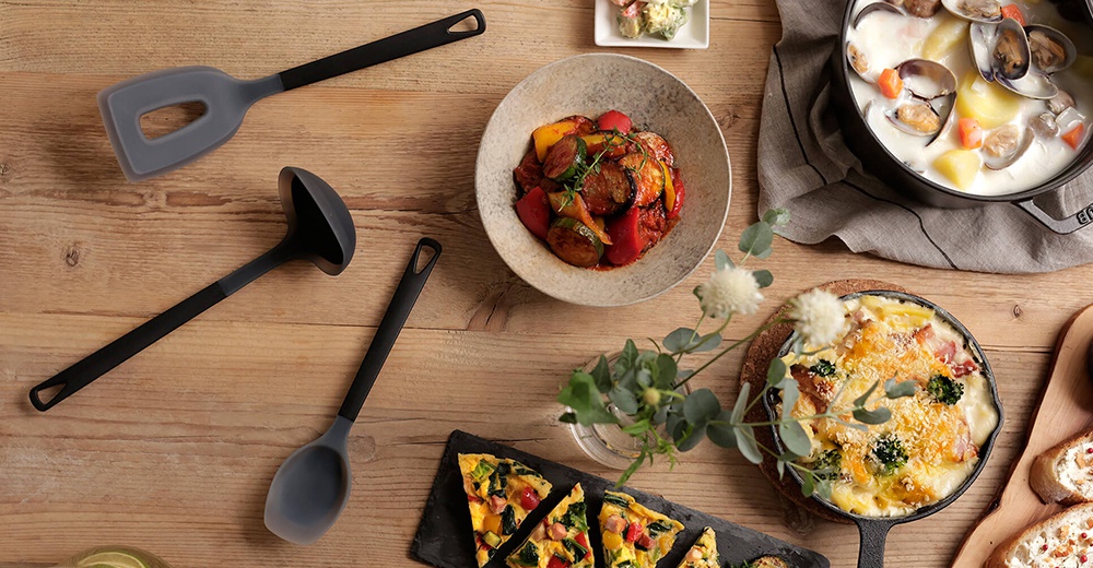 日式餐桌上擺放著一鍋海鮮燉菜、焗烤料理、蔬菜烘蛋和馬鈴薯塊，一旁還有湯勺、刮刀和麵包，營造溫馨的用餐氛圍。