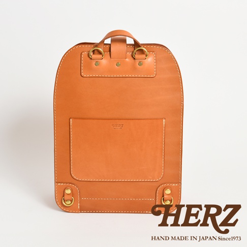 職人手作皮革商務休閒兩用後背包 R-36，採用 tan 色皮革，設計簡潔，正面有一個方形外袋，袋蓋上有品牌標誌，兩側底部及頂部均有金屬環扣，整體風格經典。