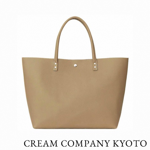 這是一款由京都職人手作的 CREAM COMPANY KYOTO 肩背手提托特包，選用輕量且耐用的 glove 牛皮革製成，呈現簡約的駝色調。包身設計寬敞，袋口設有金屬鈕扣，底部加寬的設計使其擁有良好的收納空間，適合日常休閒或商務通勤使用。