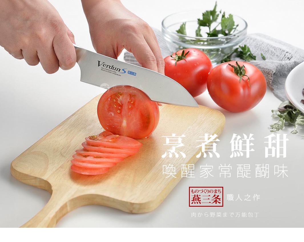 VERDUN S 不鏽鋼三德刀，刀刃鋒利，正用來切片新鮮的番茄，番茄被切成薄片放在木質砧板上，背景有其他番茄和香草。