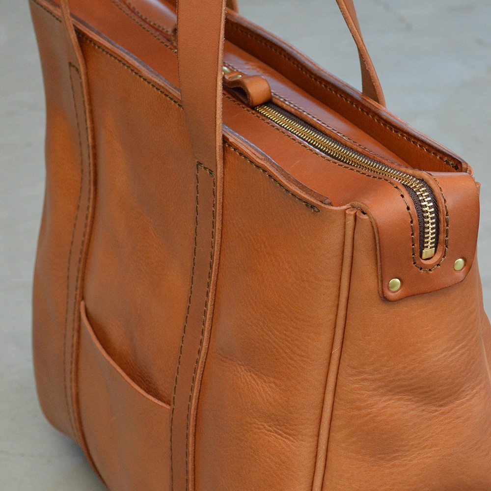 職人手作皮革Organ肩背拉鍊托特包，採用溫暖的棕褐色皮革，搭配復古黃銅色拉鍊及卯釘，包身有縫線細節，側面設有方便的插袋。