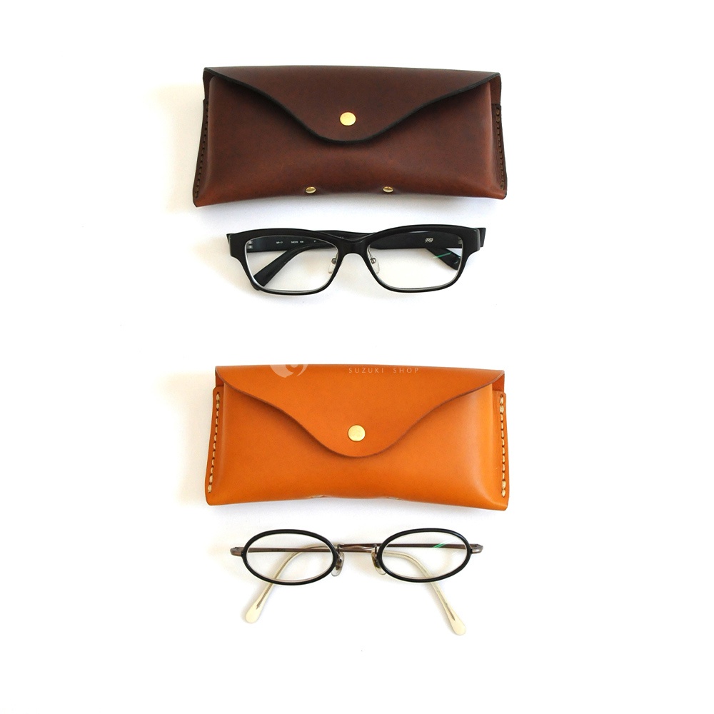 兩款不同顏色皮革製成的眼鏡盒，分別搭配一副黑色方框眼鏡和一副圓框眼鏡