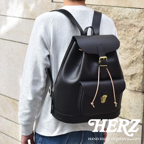 黑色皮革後背包，配有翻蓋、抽繩和金色搭扣，側面有一個帶有搭扣的貼袋。