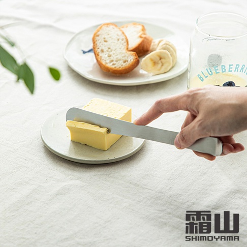 304不鏽鋼長柄包餡勺/抹刀，銀色金屬材質，刀刃平滑，用於塗抹奶油。奶油塊在白色圓盤上，背景為白色布料，盤中另有麵包片與香蕉片。