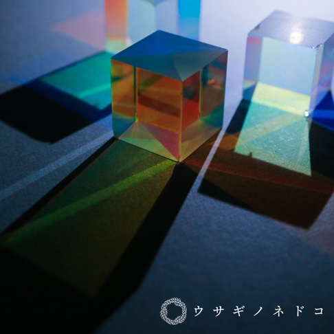 透明的合光稜鏡立方塊，表面呈現彩虹般的光澤，折射出綠、藍、橘等色彩的光影。