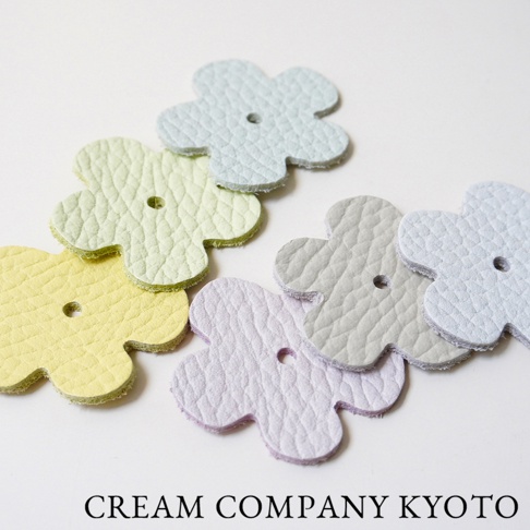 數個皮革製成的淺色花朵形狀小飾品，有淡藍、淺綠、鵝黃、淺紫、淺灰及淺藍等多種顏色，表面有細緻紋理，中央皆有圓形小孔。
