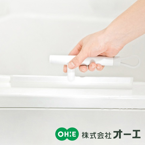 一只手握著白色 T 型把手的刮水刷，刮水條為透明矽膠材質，置於白色表面上。