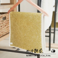 淺黃色紋理浴墊，以人字紋織法呈現，邊緣為白色滾邊，掛於粉色衣架上。