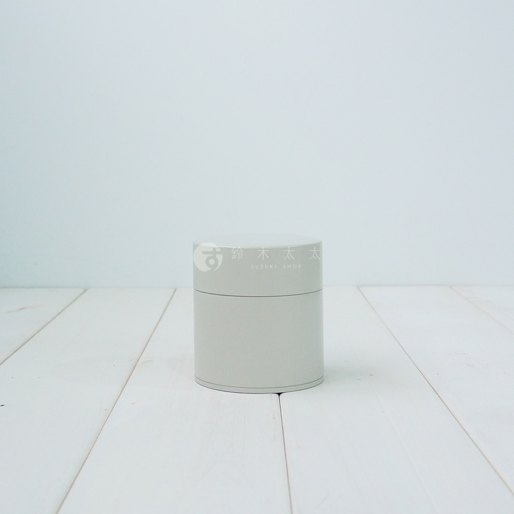 簡約的淺灰色圓柱形錫製茶葉罐，頂部有金色商標。