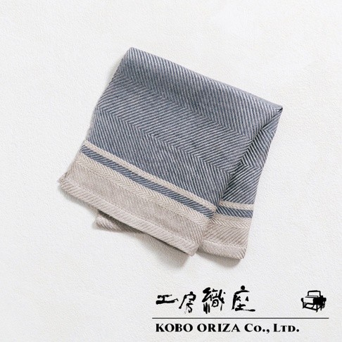 一條藍灰色純亞麻斜紋萬用廚房拭巾，帶有米色和藍色滾邊，折疊於白色背景上。